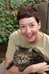 Bio photo of Becky Robinson, smiling in a pale green shirt, holding a gray and brown cat